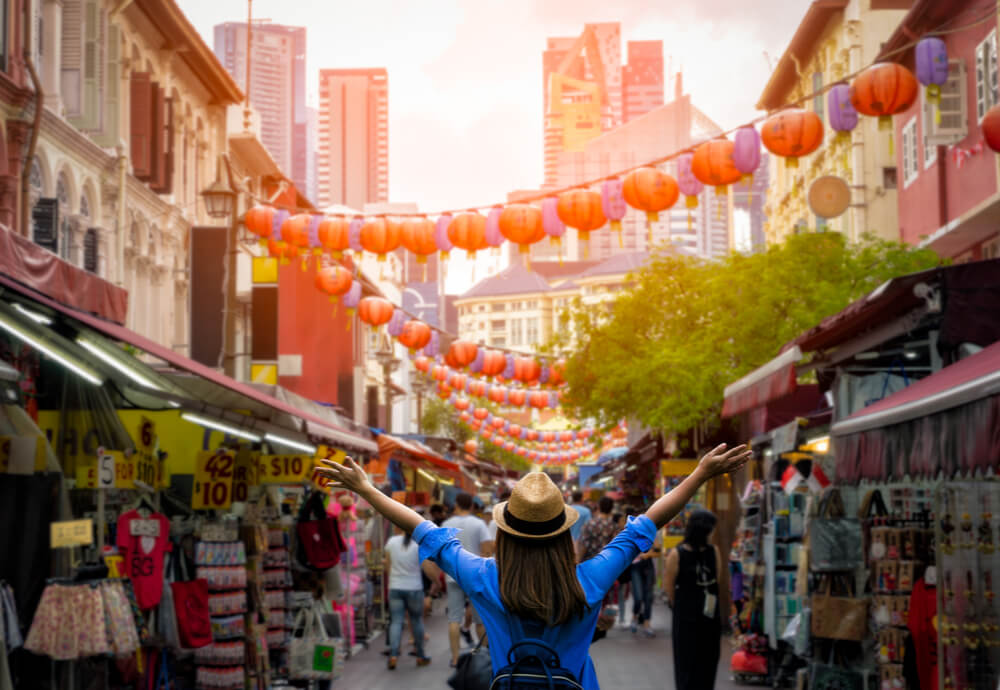 Girl in front of market with arms widespread with singapore travel insurane