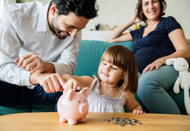Father helps little girl put coins in piggy bank