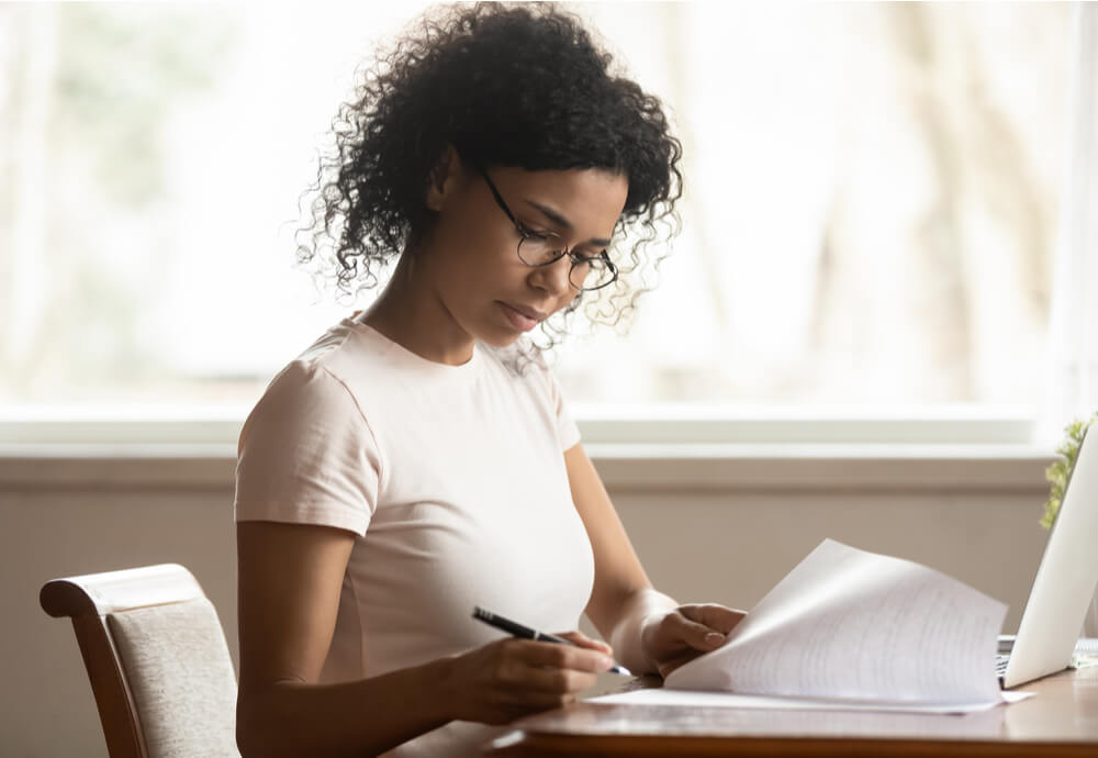 Woman sits at table in front of laptop with paperwork