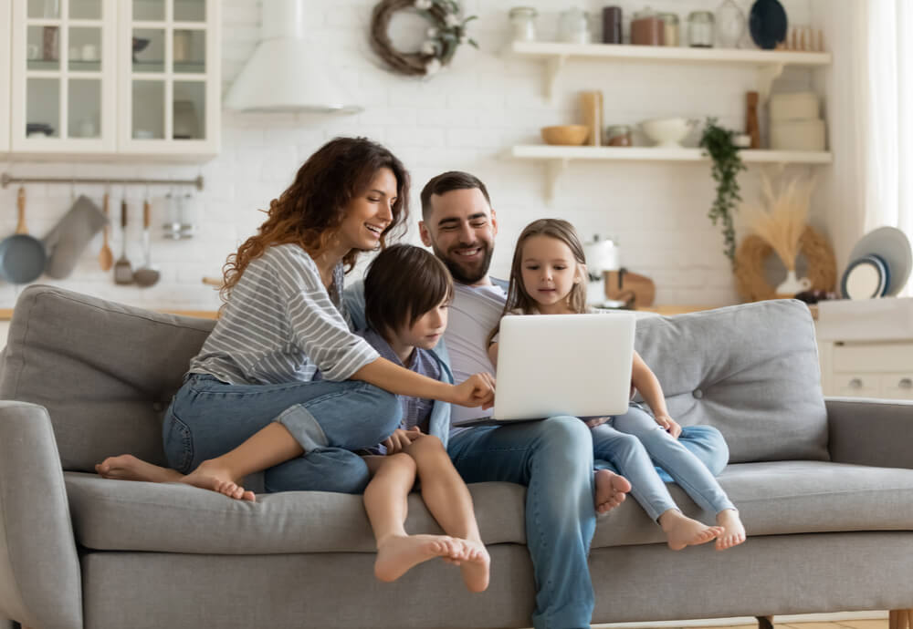 Happy family sits on couch looking at laptop