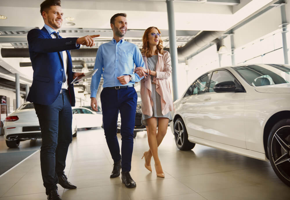 a car salesman shows a new car to a couple in a showroom