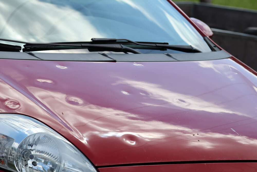 a red hatchback with hail damage on the bonnet
