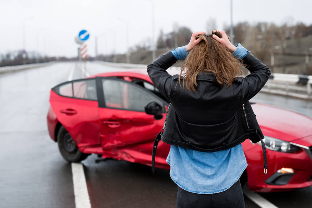 a woman looking at a damaged red car after a car crash