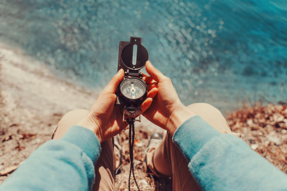 Person holding compass by the ocean
