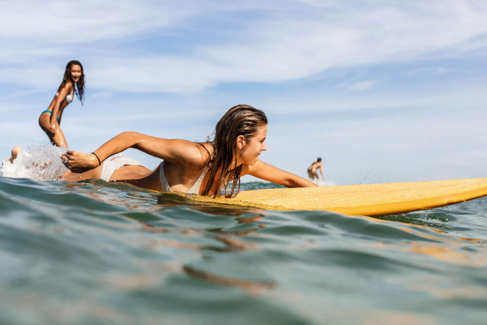 Woman with travel insurance for surfers paddling in the ocean