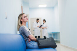 a disappointed woman waiting in a medical waiting room with doctors in the background