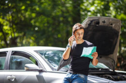 Man sitting on his car with bonnet open and calling his car insurer