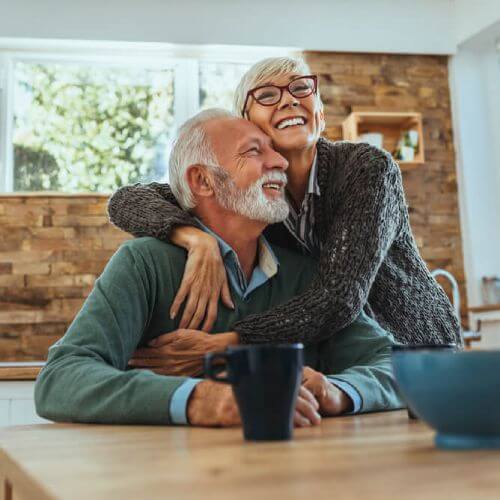 Older couple with silver health insurance hug in kitchen