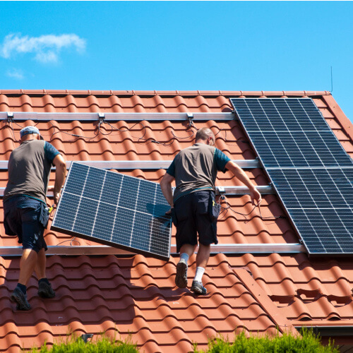 Two workers installing solar panels on a home