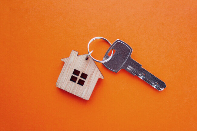 Key with wooden home keyring in front of orange background