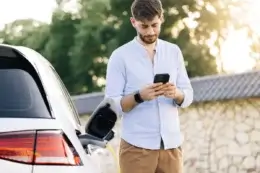 Man holding a phone next to charging EV